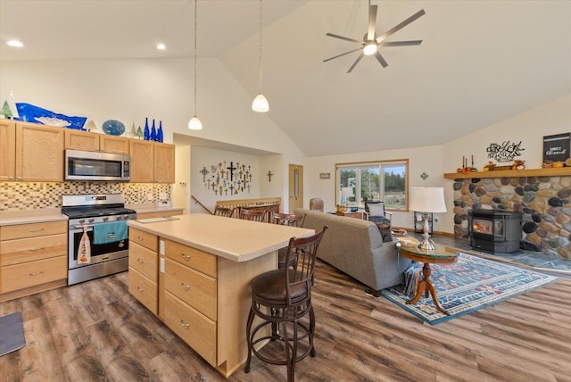 kitchen with a wood stove, dark wood-type flooring, a kitchen breakfast bar, a kitchen island, and stainless steel appliances