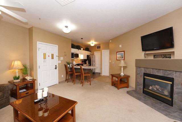 carpeted living room with ceiling fan and a tile fireplace