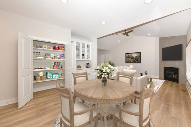 dining room with a tile fireplace, light wood-type flooring, vaulted ceiling, and ceiling fan