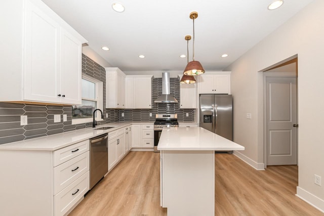 kitchen with wall chimney exhaust hood, hanging light fixtures, stainless steel appliances, light hardwood / wood-style floors, and a kitchen island