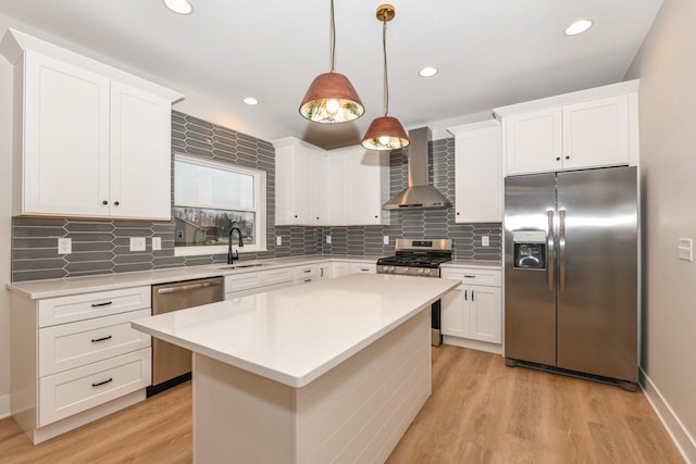 kitchen featuring stainless steel appliances, wall chimney range hood, light hardwood / wood-style flooring, a center island, and hanging light fixtures