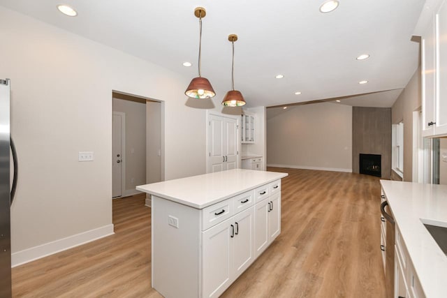 kitchen with a fireplace, white cabinets, hanging light fixtures, and light hardwood / wood-style flooring