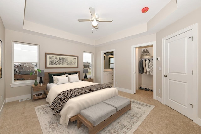 bedroom featuring light carpet, a walk in closet, a tray ceiling, and ceiling fan