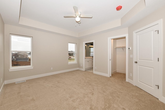 unfurnished bedroom featuring ceiling fan, ensuite bath, light carpet, and a tray ceiling