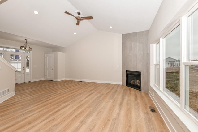 unfurnished living room with ceiling fan with notable chandelier, light wood-type flooring, lofted ceiling, and a tiled fireplace