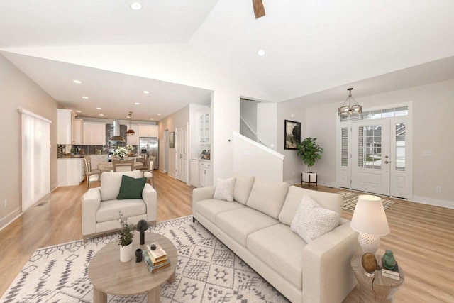 living room with vaulted ceiling, an inviting chandelier, and light hardwood / wood-style flooring