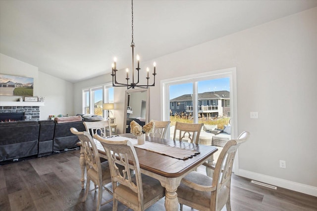 7759 Sunstone Ct, De Pere, WI 54115 - dining space with a chandelier, vaulted ceiling, dark wood-style flooring, baseboards, and a warm lit fireplace