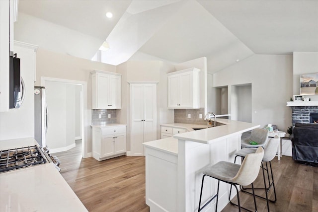 7759 Sunstone Ct, De Pere, WI 54115 - kitchen with a sink, vaulted ceiling, light wood-style floors, a breakfast bar, and tasteful backsplash