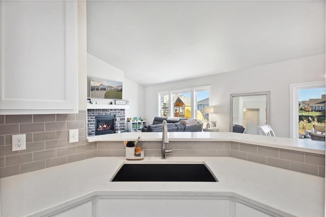 7759 Sunstone Ct, De Pere, WI 54115 - kitchen with a sink, decorative backsplash, white cabinetry, open floor plan, and a glass covered fireplace