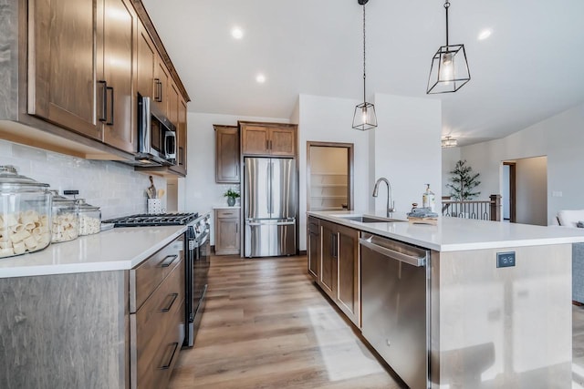 kitchen with appliances with stainless steel finishes, a kitchen island with sink, sink, pendant lighting, and light hardwood / wood-style flooring