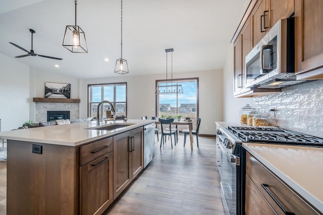 kitchen with sink, pendant lighting, a center island with sink, stainless steel appliances, and a stone fireplace