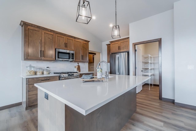 kitchen with stainless steel appliances, vaulted ceiling, a kitchen island with sink, light hardwood / wood-style flooring, and hanging light fixtures