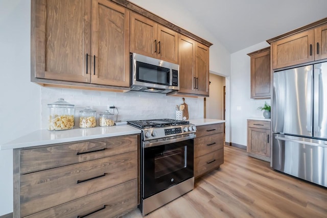 kitchen featuring backsplash, stainless steel appliances, lofted ceiling, and light hardwood / wood-style floors