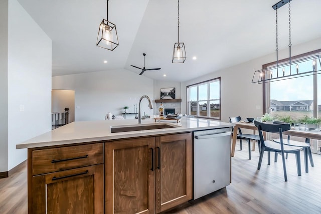 kitchen with light wood-type flooring, stainless steel dishwasher, vaulted ceiling, a kitchen island with sink, and sink