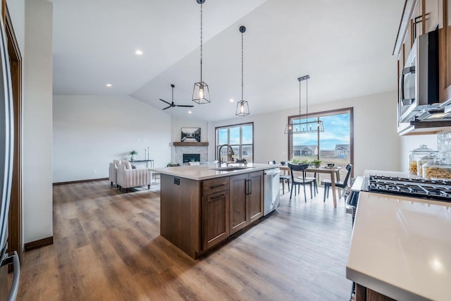 kitchen with stainless steel appliances, hardwood / wood-style floors, vaulted ceiling, decorative light fixtures, and a center island with sink