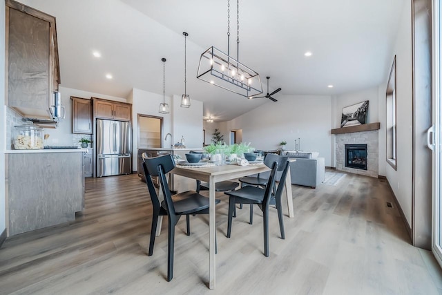 dining room featuring light hardwood / wood-style flooring, vaulted ceiling, and a tiled fireplace