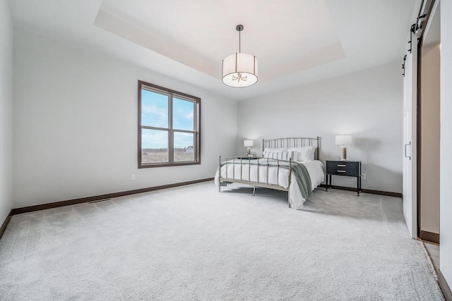 carpeted bedroom featuring a raised ceiling and a barn door