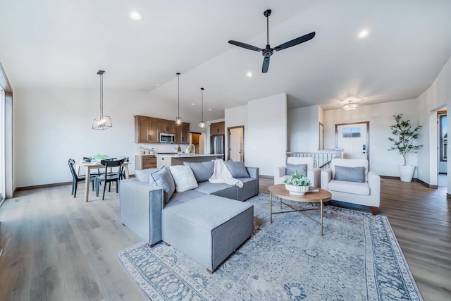 living room with ceiling fan, light hardwood / wood-style flooring, vaulted ceiling, and sink