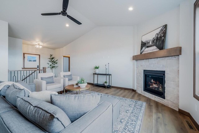 living room with a stone fireplace, ceiling fan, vaulted ceiling, and hardwood / wood-style flooring