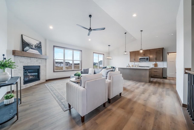 living room featuring a fireplace, ceiling fan, hardwood / wood-style floors, and vaulted ceiling