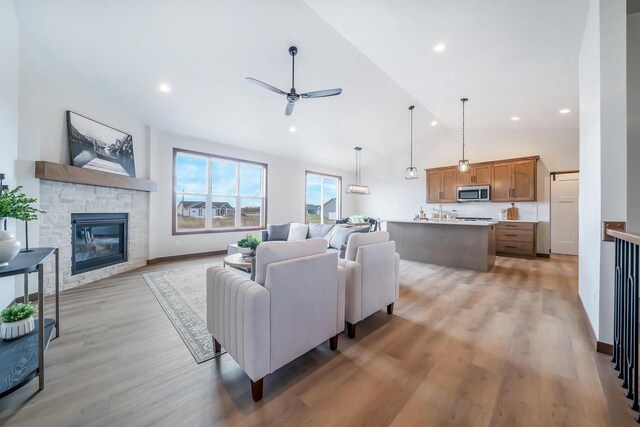 living room featuring ceiling fan, sink, a stone fireplace, high vaulted ceiling, and light hardwood / wood-style floors