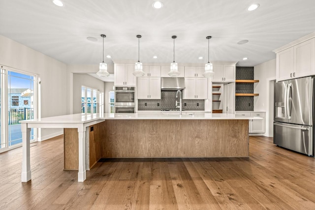 kitchen with hanging light fixtures, stainless steel appliances, hardwood / wood-style floors, a spacious island, and white cabinets