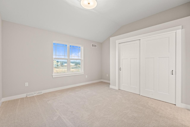 unfurnished bedroom with light colored carpet, a closet, and lofted ceiling