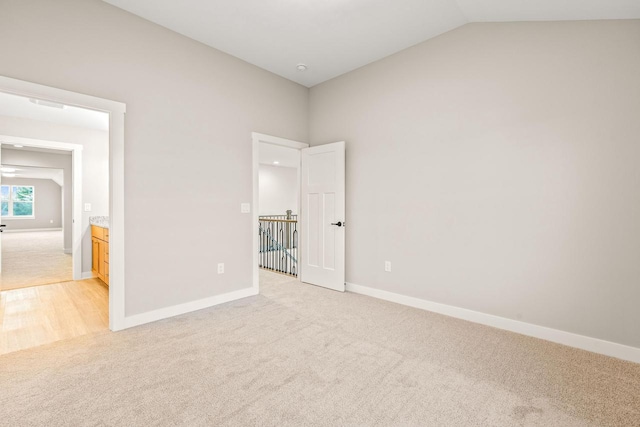 unfurnished bedroom featuring lofted ceiling, light carpet, and ensuite bath