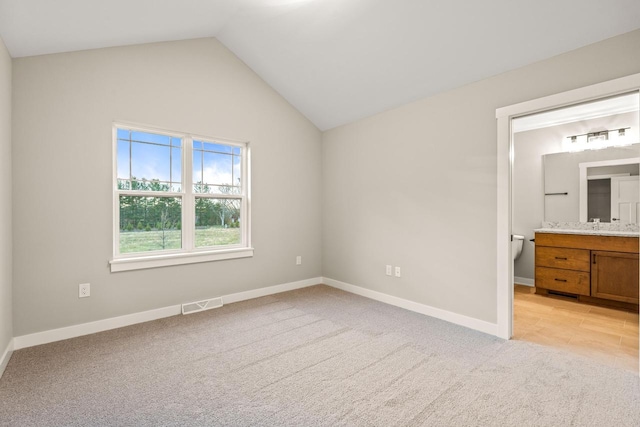 unfurnished bedroom featuring light colored carpet, lofted ceiling, and ensuite bath