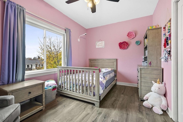 bedroom with ceiling fan, wood-type flooring, and a crib