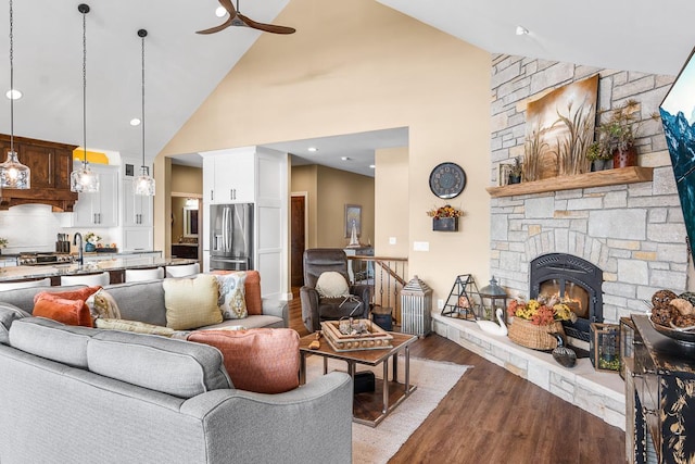 living room with ceiling fan, sink, high vaulted ceiling, light hardwood / wood-style floors, and a stone fireplace