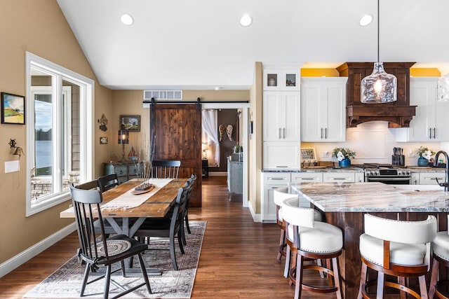 kitchen with white cabinets, a barn door, decorative light fixtures, dark hardwood / wood-style floors, and light stone countertops