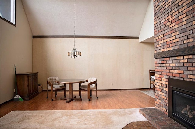 dining room featuring hardwood / wood-style flooring, a notable chandelier, a fireplace, and high vaulted ceiling