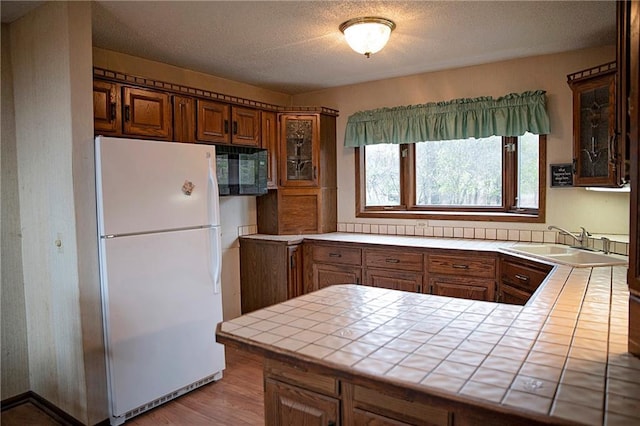 kitchen with kitchen peninsula, tile counters, white fridge, and sink