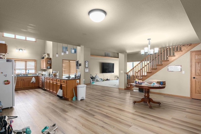 kitchen featuring kitchen peninsula, pendant lighting, light hardwood / wood-style flooring, a notable chandelier, and white fridge