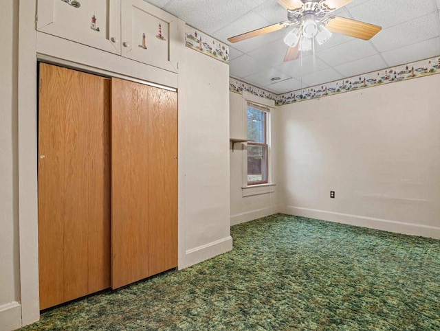 unfurnished bedroom with dark carpet, a drop ceiling, and ceiling fan