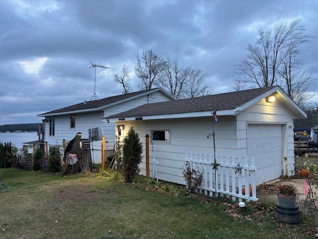 rear view of property featuring a garage, a water view, a lawn, and roof with shingles