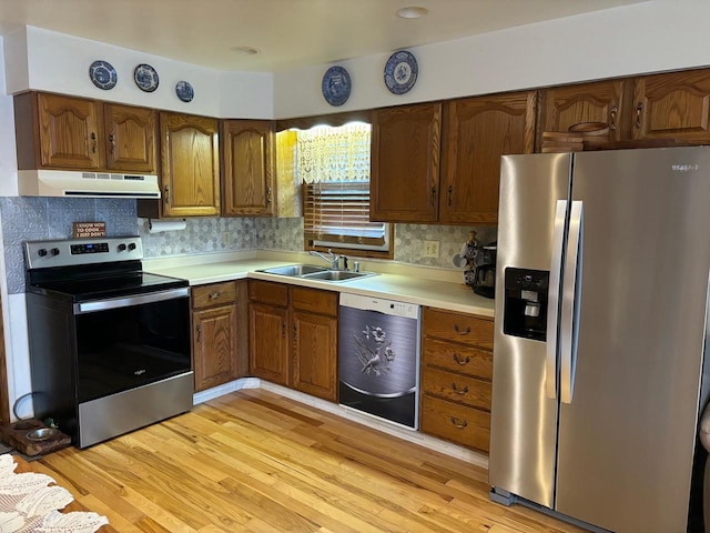 kitchen featuring stainless steel appliances, light countertops, light wood-style floors, a sink, and under cabinet range hood