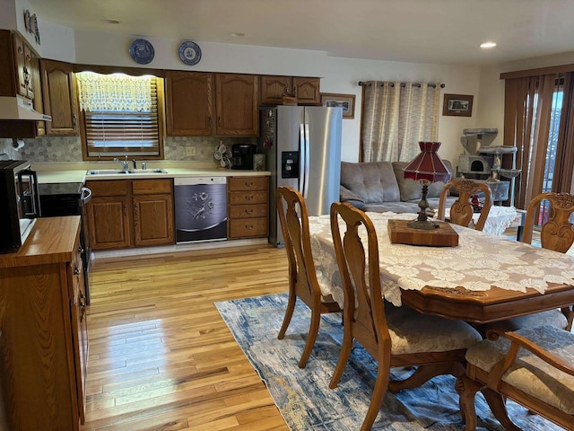 kitchen featuring dishwashing machine, a sink, butcher block countertops, under cabinet range hood, and stainless steel fridge with ice dispenser