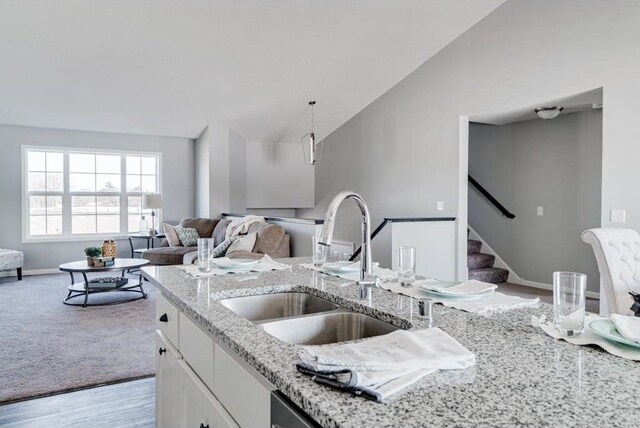 kitchen featuring lofted ceiling, sink, hanging light fixtures, light stone countertops, and white cabinets