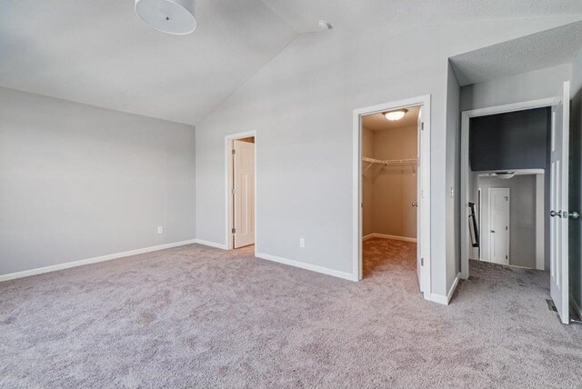 unfurnished bedroom featuring lofted ceiling, a closet, a spacious closet, and light carpet