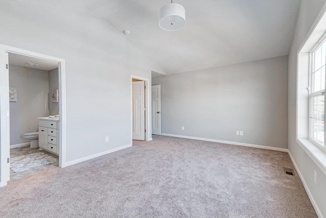 unfurnished bedroom featuring light colored carpet, multiple windows, connected bathroom, and vaulted ceiling