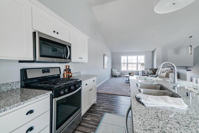 kitchen featuring appliances with stainless steel finishes, lofted ceiling, white cabinets, light stone counters, and sink