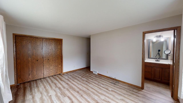 unfurnished bedroom with ensuite bath, a closet, sink, and light hardwood / wood-style flooring