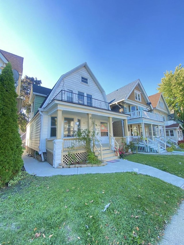 view of front of home with covered porch, a gambrel roof, a balcony, and a front yard
