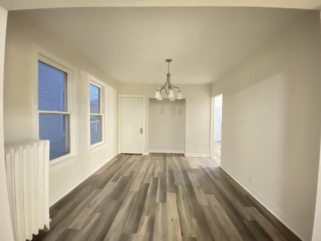 unfurnished dining area featuring radiator heating unit, a chandelier, dark wood-style flooring, and baseboards