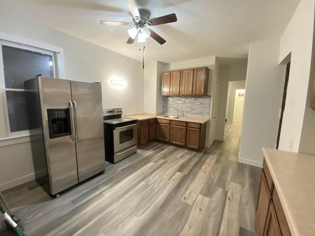 kitchen with stainless steel appliances, ceiling fan, brown cabinetry, light wood finished floors, and backsplash