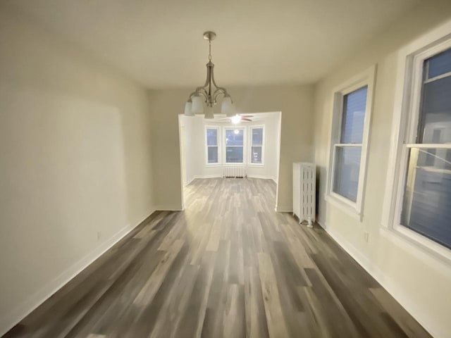 unfurnished dining area featuring radiator, a chandelier, dark wood finished floors, and baseboards