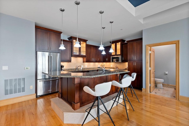 kitchen with a kitchen breakfast bar, pendant lighting, stainless steel appliances, and light hardwood / wood-style floors