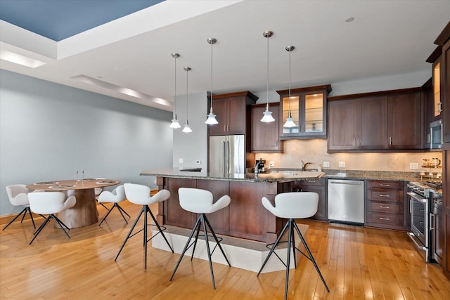 kitchen featuring dark stone counters, a breakfast bar area, decorative light fixtures, light hardwood / wood-style floors, and stainless steel appliances